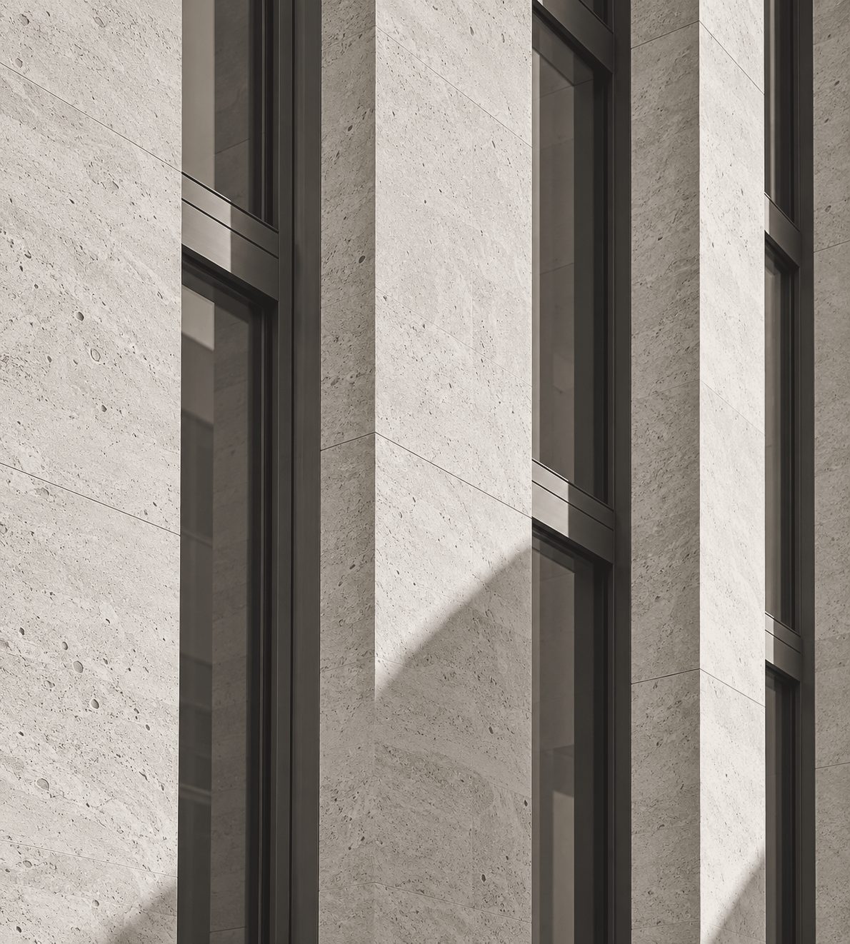 Travertine façade with tall recessed windows in bronze frames, in low sun.
